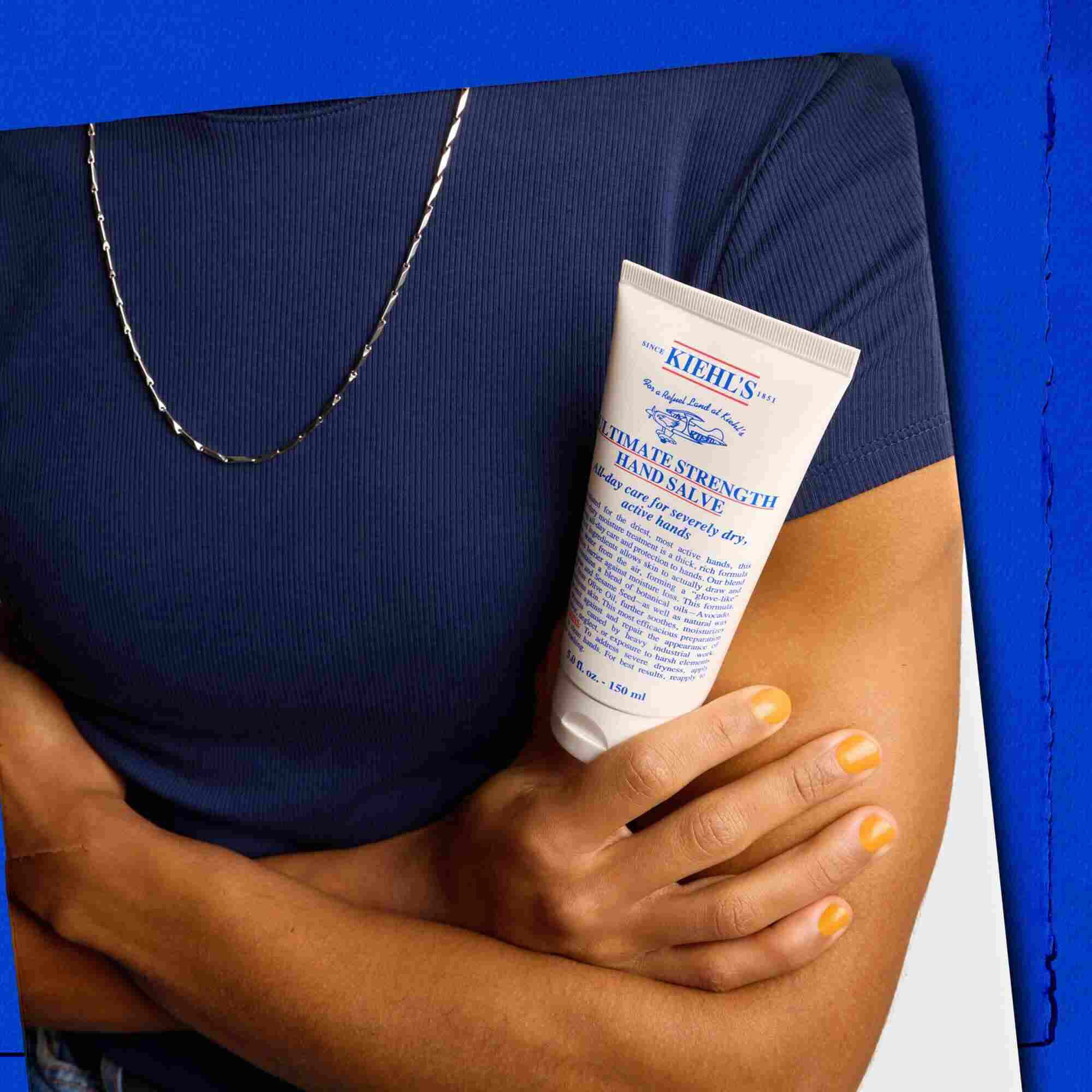Modell, aki egy tubus Kiehl's Ultimate Strength Hand Salve intenziv kezkremet tart