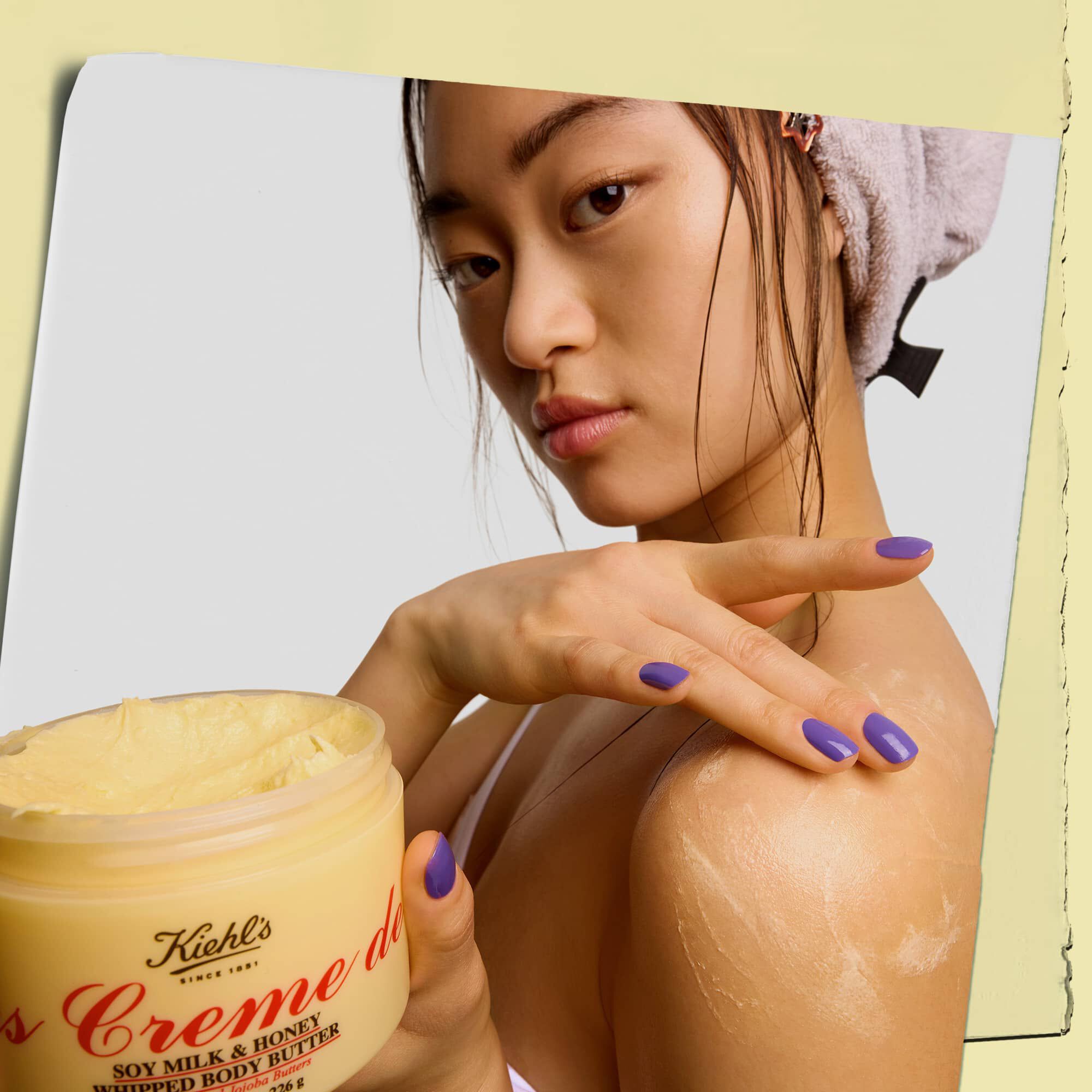 Modell, amint egy tegelyt tart es felviszi a Kiehl's Creme de Corps Whipped Butter testvajat