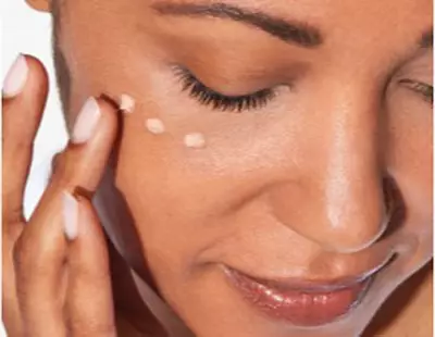 A close-up of a person's face as they gently apply a cream or lotion under their eye with their fingers.