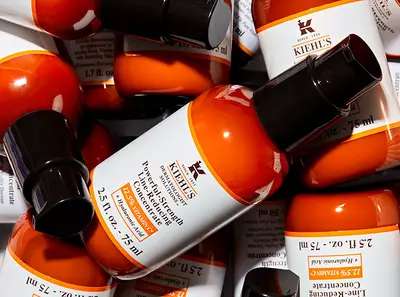 Kiehl's narancsszinu hajapolo szerumok egy kupacban, fekete kupakokkal es feher cimkekkel.