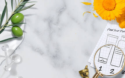 A flat lay featuring a marble surface with botanical elements like olive branches and marigold petals, along with a mortar and pestle. There's a magnifying glass over a grid paper with markings of product formulas, and a decorative border with space for text.