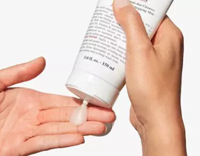 A hand is dispensing a small amount of cream from a white tube onto another hand.