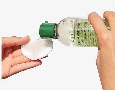 Kezben tartott Kiehl's arctisztito tonik palack, vattakorongra ontve.