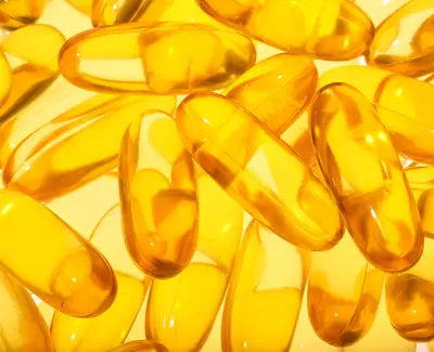 A close-up view of numerous translucent yellow gel capsules arranged closely together on a light background.