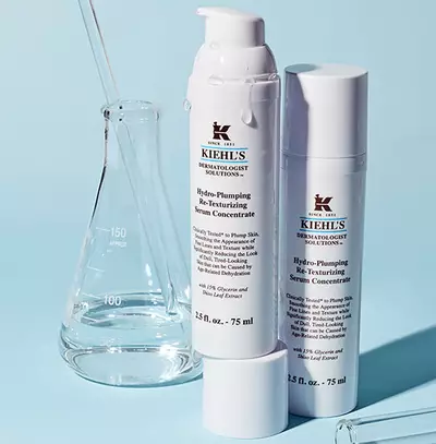 Ket Kiehl's bőrfe rejuvenalo szerum koncentratum, pipettaval es laboratoriumi uveggel diszitett hatterben.